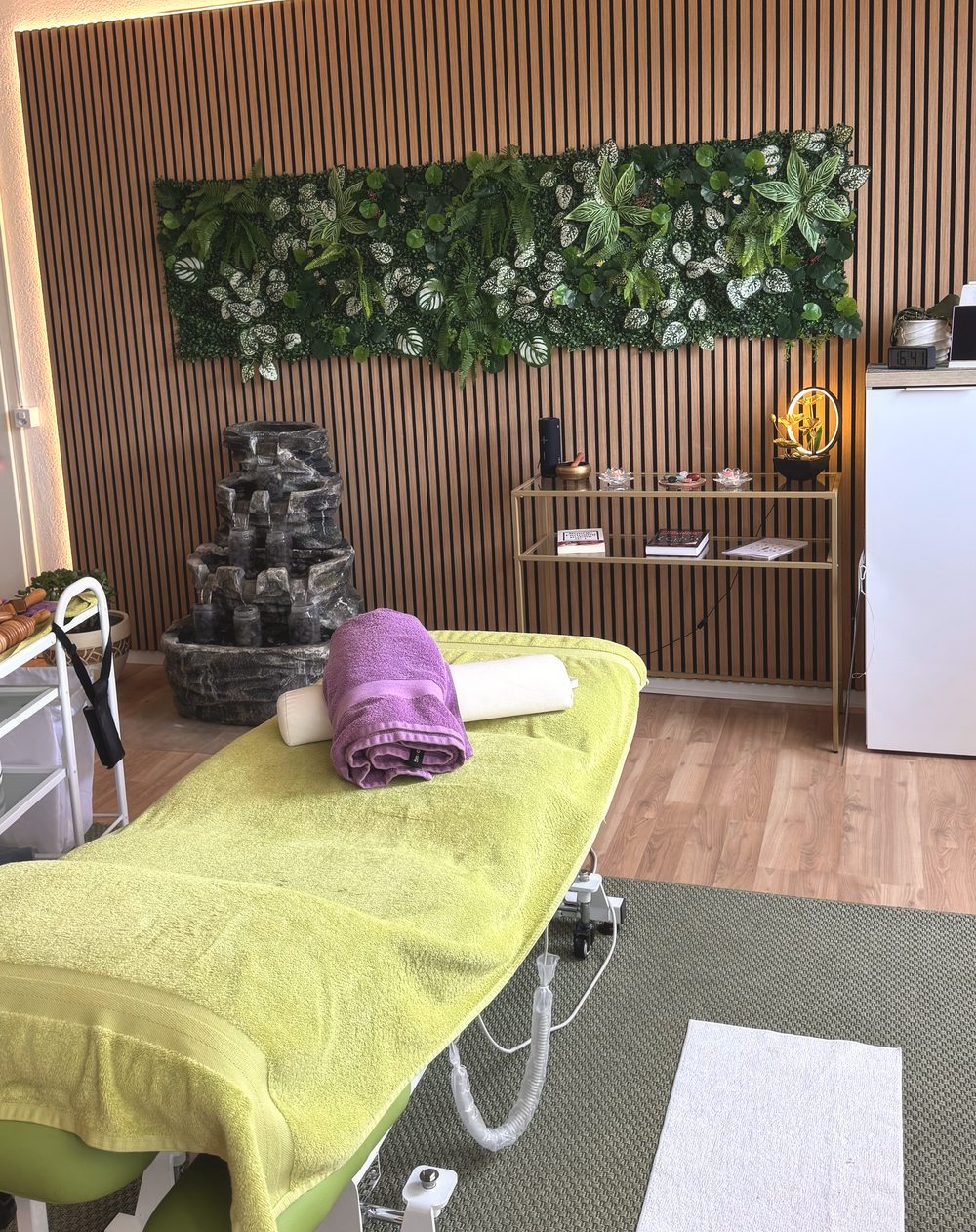 La salle de soin : table de massage devant le mur végétal et la paroi en tasseaux de bois